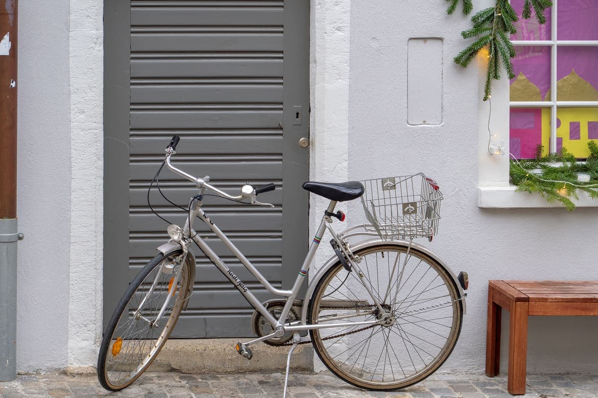 A silver city bike with a basket parked by a wall trimmed with festive greenery